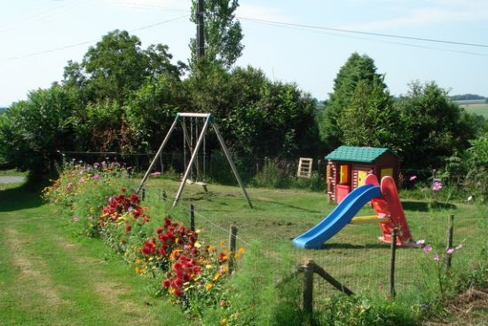 Espace jeux avec quelques aménagements : salon de jardin, parasol, barbecue, balançoires, terrain clos, pelouse non close, table ping-pong, espace jeux commun aux 2 gîtes